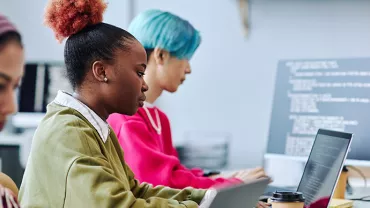 Three people working on laptops in an office setting.