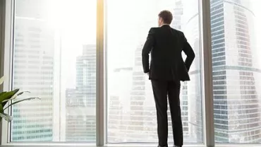 A man in a suit looking out at a cityscape through a large window.